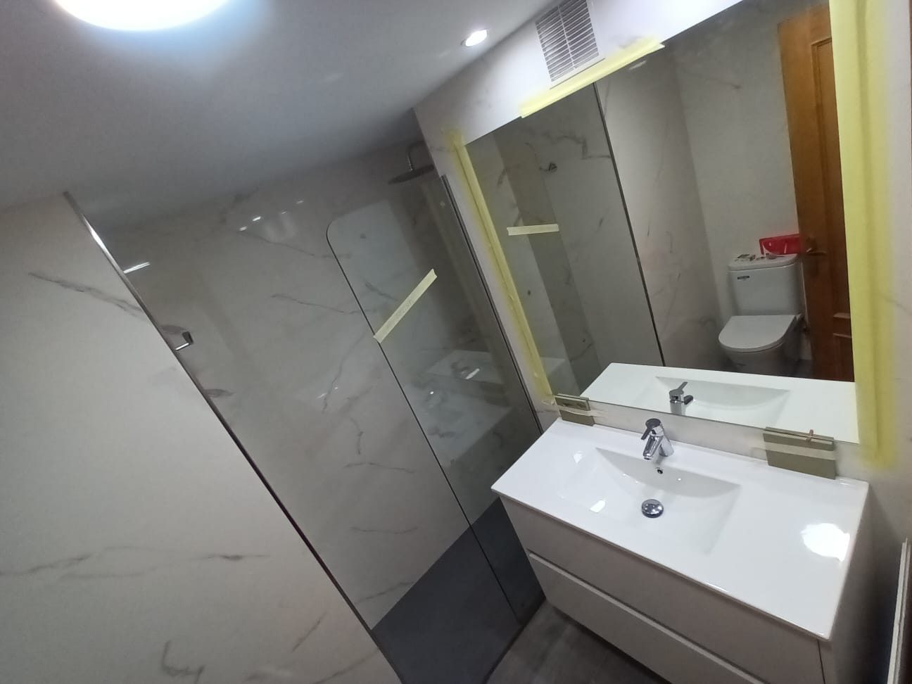 Baño reformado en mármol blanco con mampara